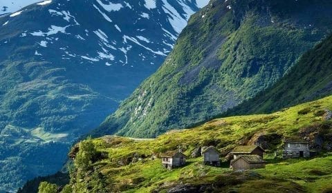 Wooden cabins with grass rooftops in the high mountains, snow on the mountain peaks